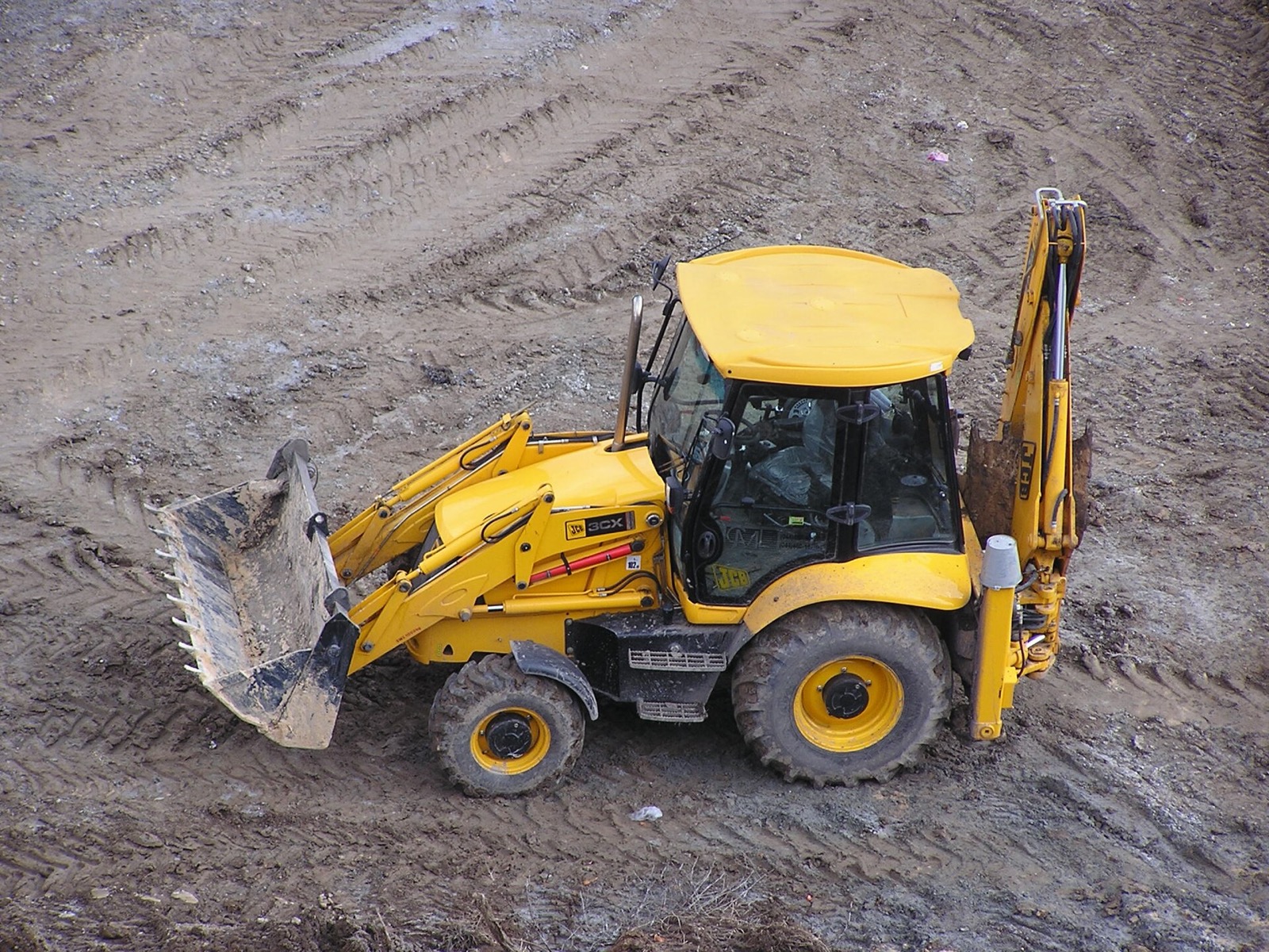 A yellow JCB 3CX backhoe loader on a muddy site: the digger that made the Bamford family's company, where Lord Bamford named his youngest son George joint chairman from October 2026