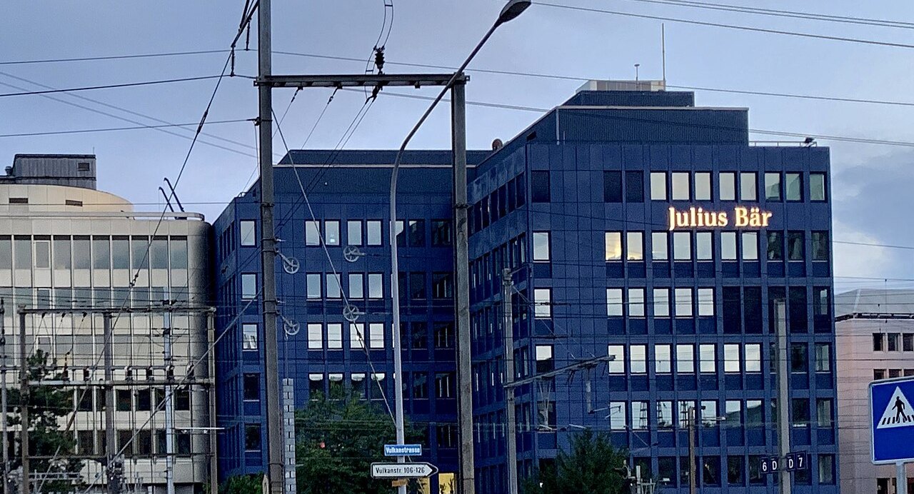 A Julius Bär office building on Hohlstrasse in Zürich-Altstetten at dusk, its lit Julius Bär sign above the railway lines. The Swiss private bank's Singapore trust company lost the Moss Trust case in the Singapore High Court in October 2026