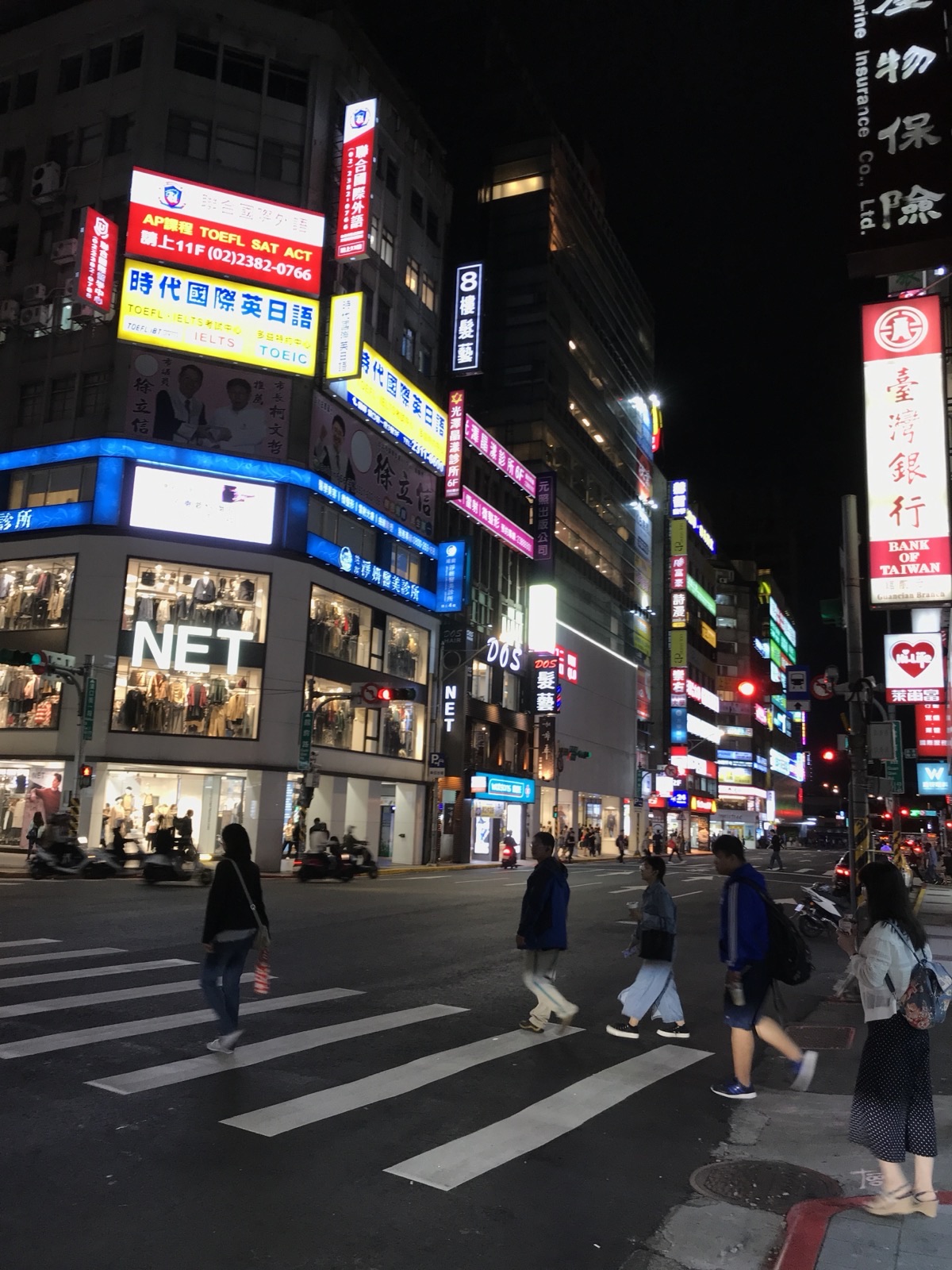 Guanqian Road, Taipei, at night in October 2018, lit by cram-school and clinic signs with the Bank of Taiwan Guanqian branch sign at right — the block opposite Taipei Main Station where the NOVA co-founder's shopfront, rented to Starbucks, has passed through three landlords since 2021