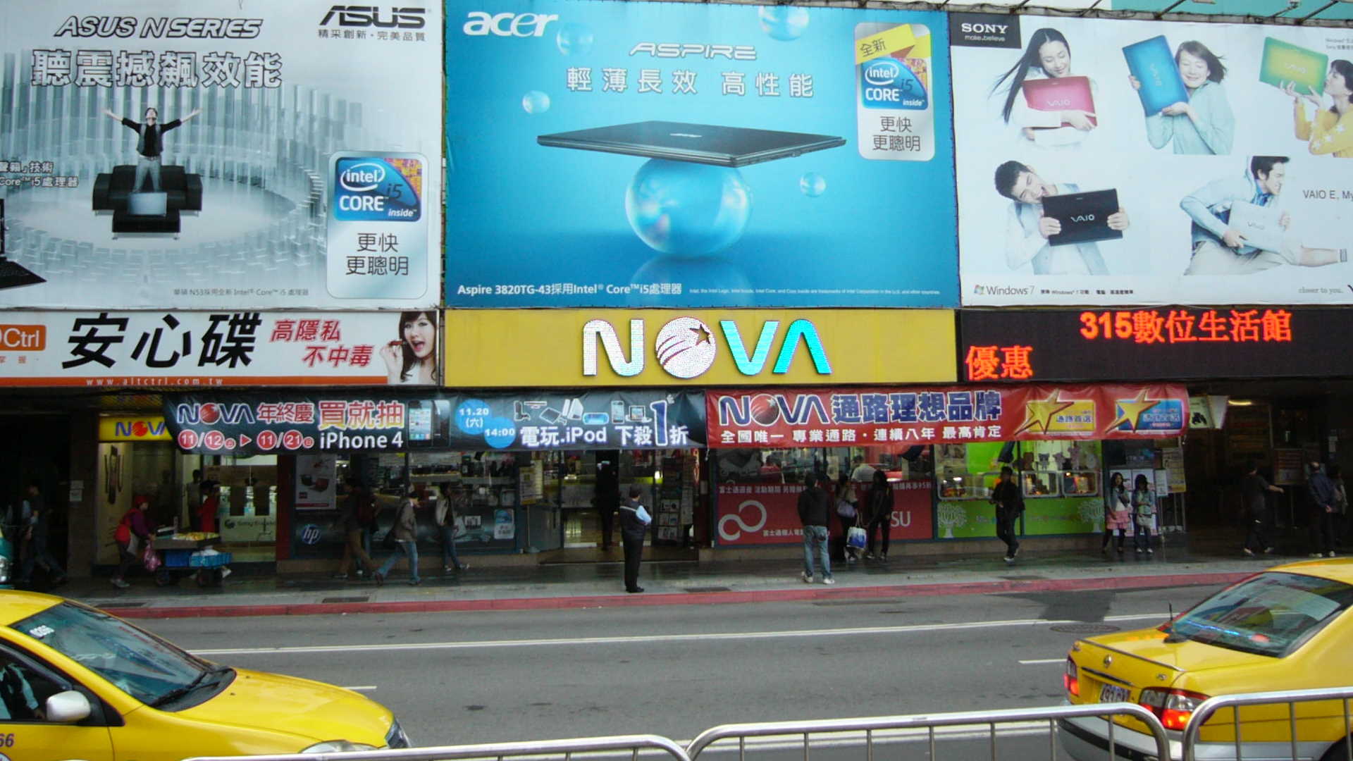 The NOVA computer mall's Taipei Station store on Guanqian Road in November 2010, its neon NOVA sign above the shopfront and yellow taxis passing — the chain Chung Chiung-ming co-founded in 1996, whose three floors at No. 26 Guanqian Road are the estate his family has litigated since 2012